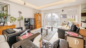A modern living room with a sofa, coffee table, and a television. There is a large window with a view of buildings. - Beautiful 1 Bed on the River (London)