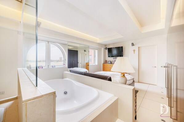Relax in a serene bedroom with a bathtub, flat-screen TV, and city views.