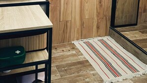 Une cuisine avec un pare-feu en bois, un saladier noir posé sur une table, un récipient vert et un tapis à rayures sur le sol.