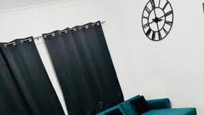 A living room with a teal sofa, a black coffee table, a dining table with chairs, and a black clock on the wall. - Elegant 2-bedroom Apartment Near City Centre (Birmingham)