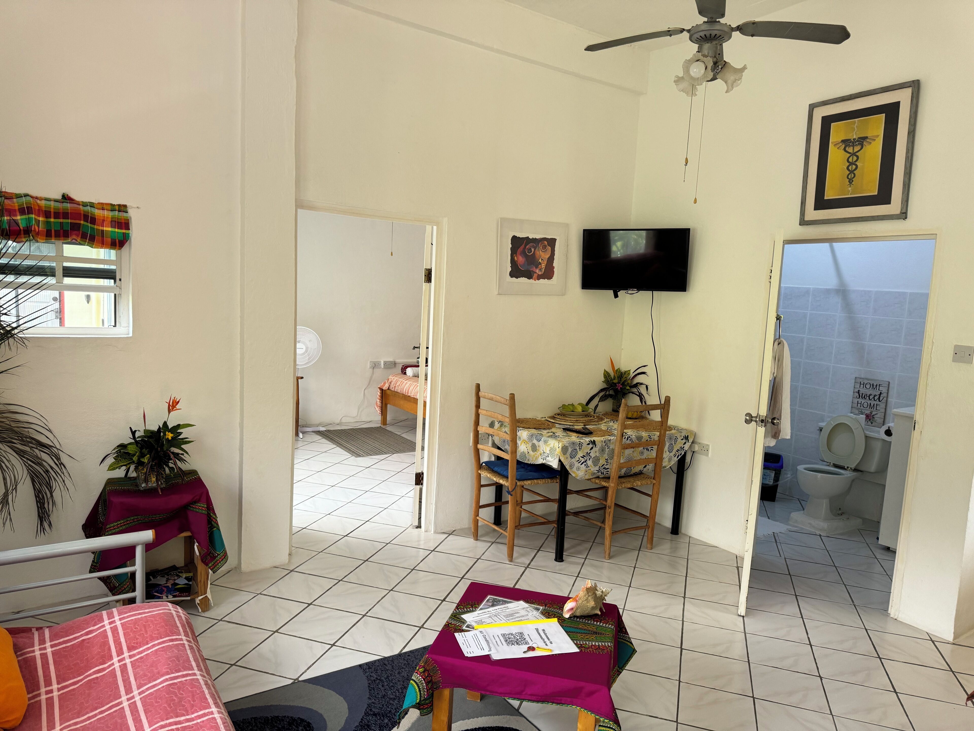 Une pièce comprenant un lit, une table à manger avec des chaises, un téléviseur fixé au mur et une salle de bain visible à travers une porte ouverte.