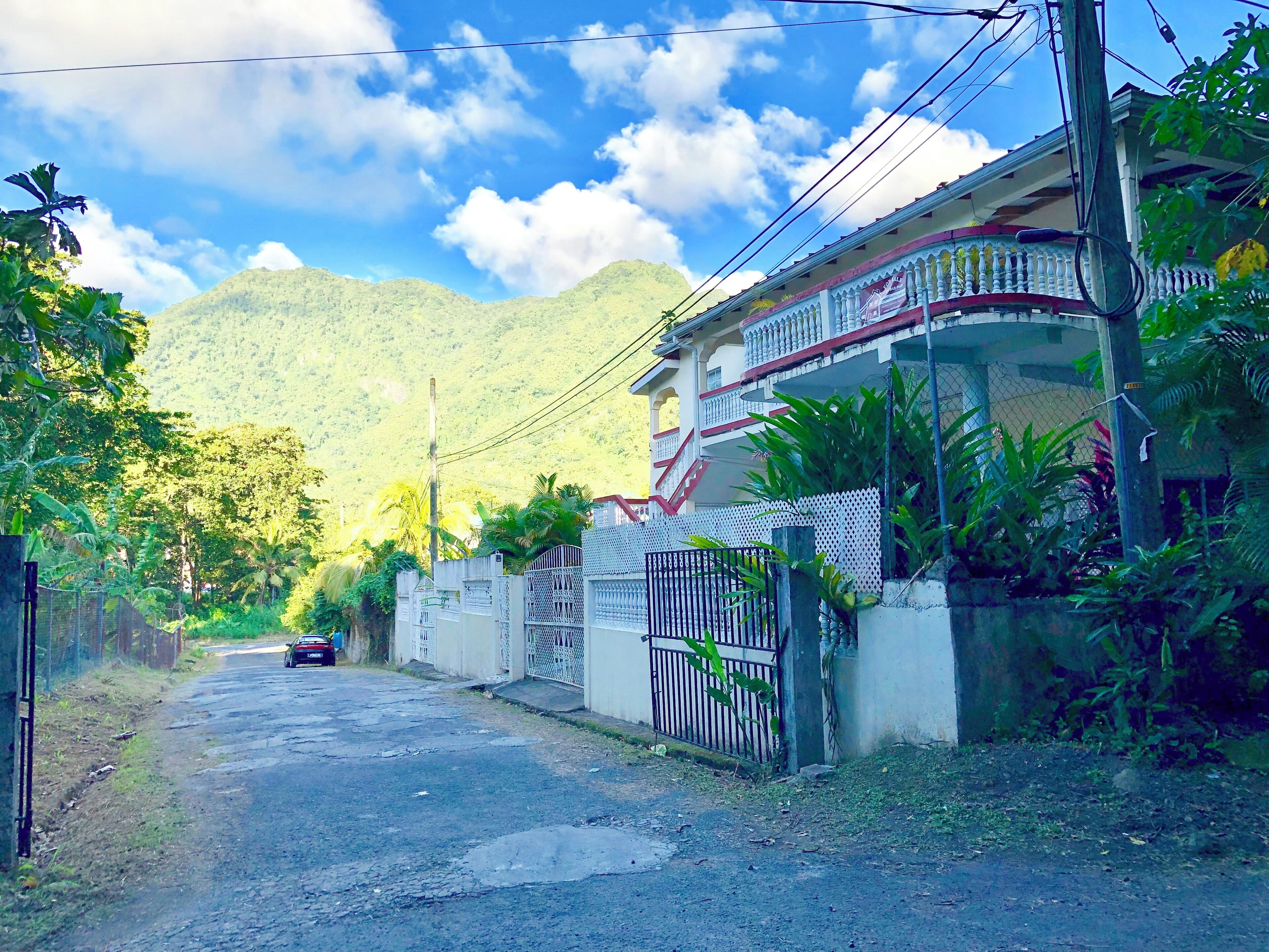 A residential street with a house featuring a gated entrance, a balcony, and a mountain backdrop.