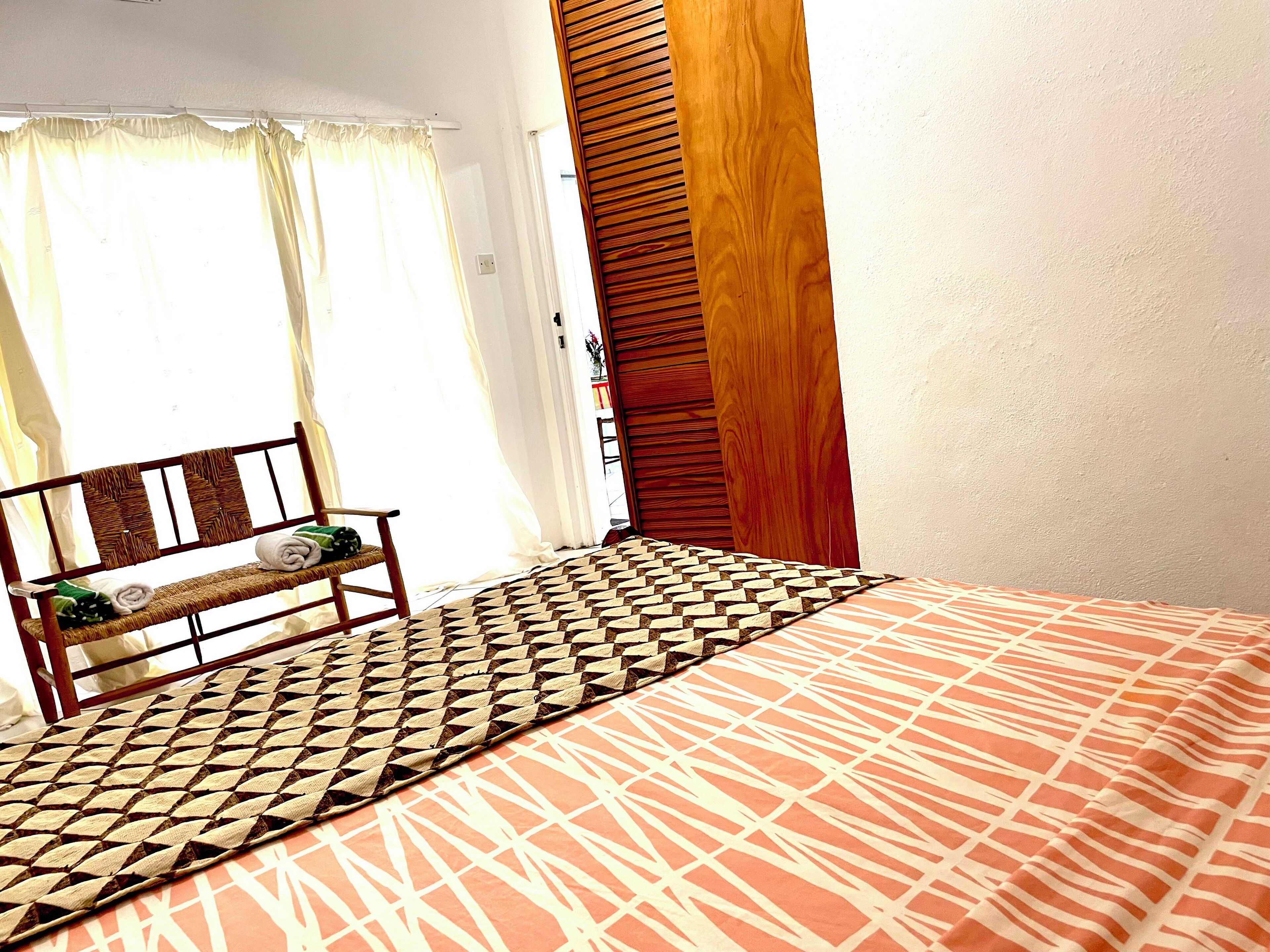 A room with a bed, a bench with towels, a window with curtains, and a wooden panel wall.