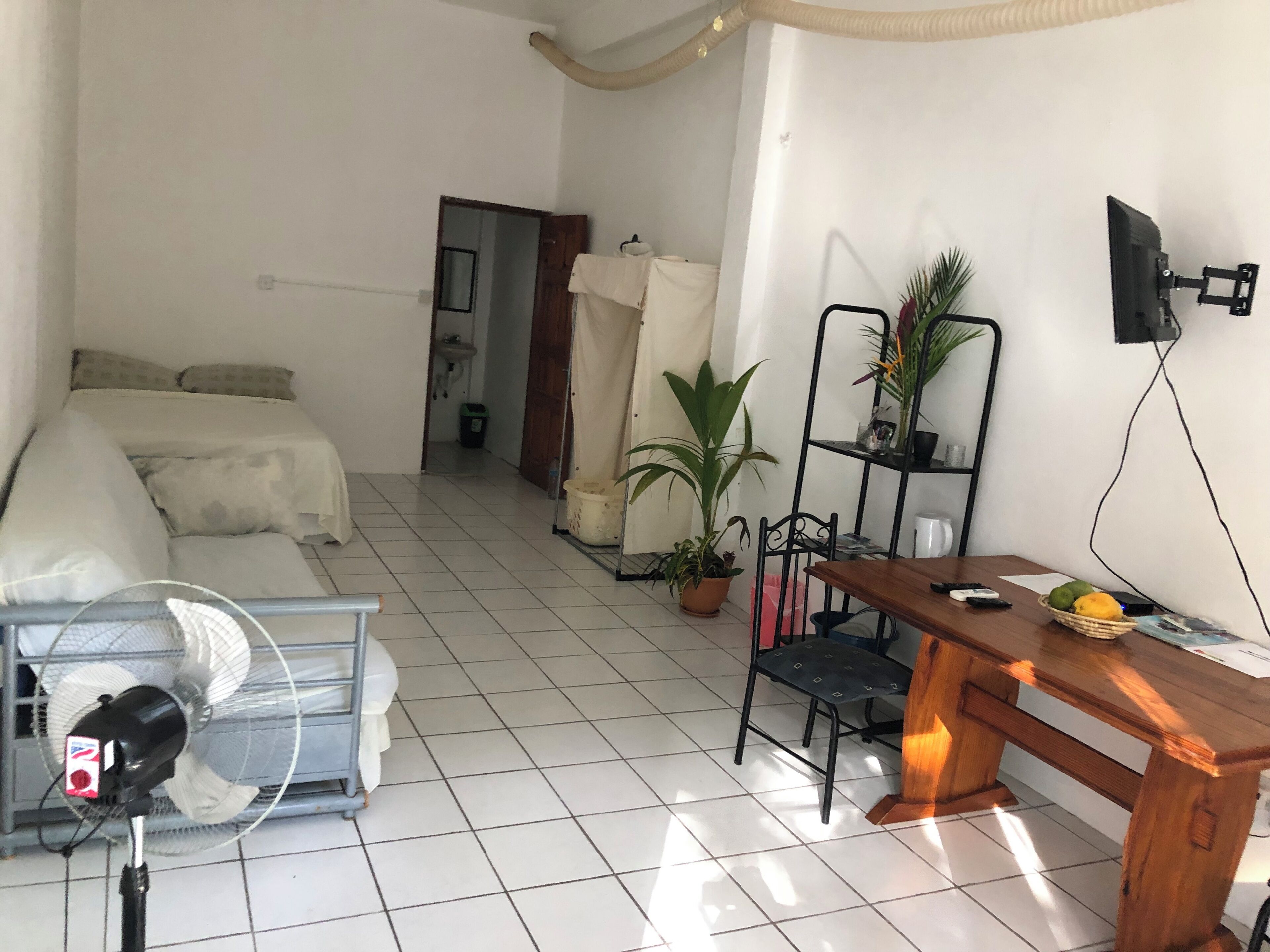 A small, clean room with a bed, a desk, a chair, a fan, and a TV on the wall.