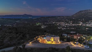 A coastal property with a modern house, a driveway, and a view of the sea and distant hills.