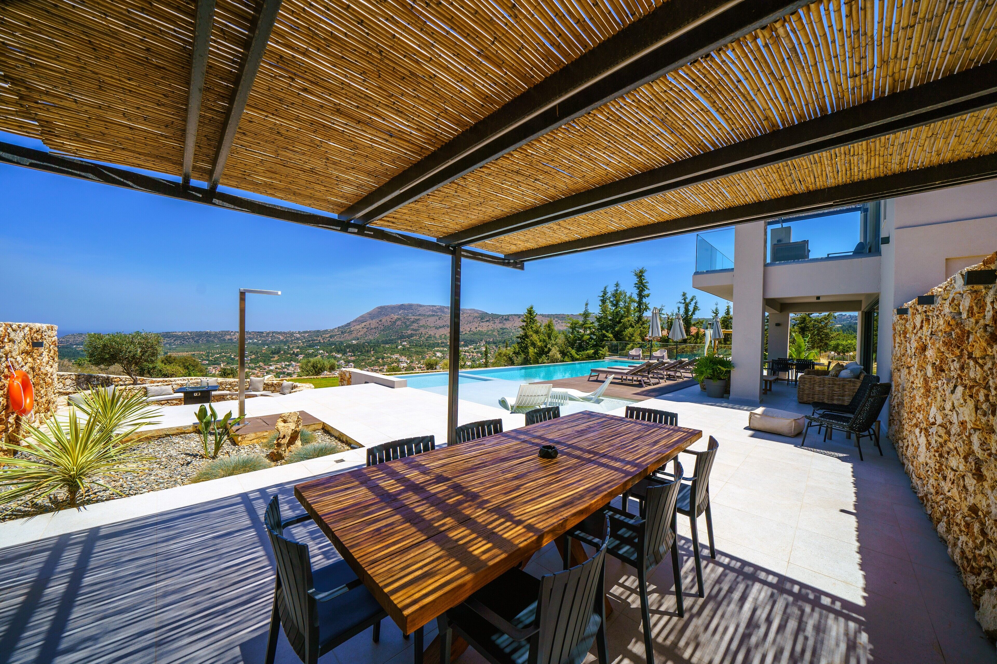An outdoor patio with a wooden table and chairs, a pool, and a view of the mountains.