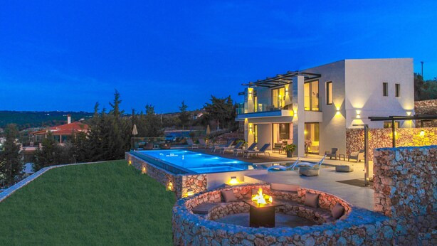 A modern house with a swimming pool, outdoor seating, and a stone fire pit.