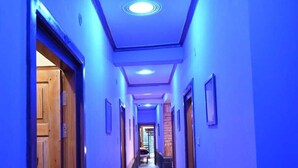 A hallway with a blue-lit ceiling, wooden doors, and a tiled floor. - Hotel Lohaghat Regency  (Lohaghat)