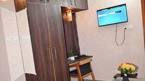 A bedroom with a bed, a wardrobe, a desk, a TV, and a vase with flowers. - Hotel Lohaghat Regency  (Lohaghat)