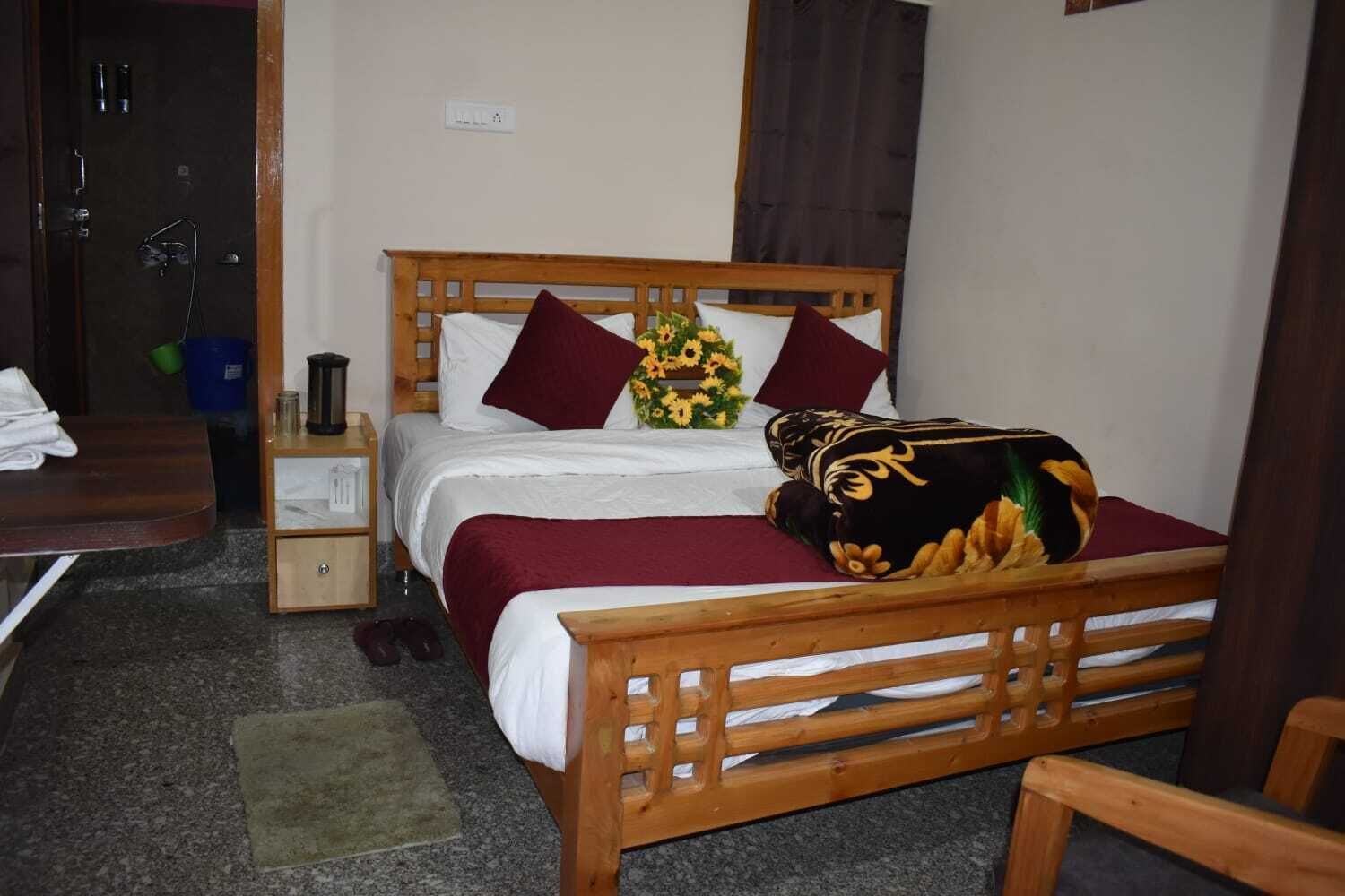 Een houten bed met een kussen in rood en zwart patroon, wit beddengoed en een vaas met zonnebloemen.