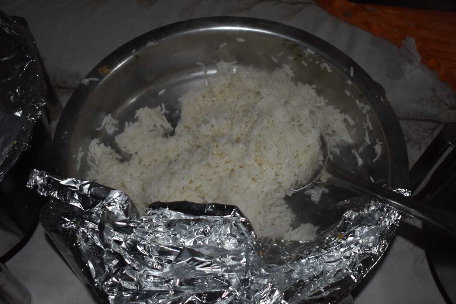 A stainless steel bowl containing white rice, placed on a table with aluminum foil underneath.