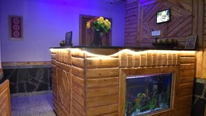 A wooden reception desk with a built-in aquarium, a framed picture, and a vase with flowers. - Hotel Lohaghat Regency  (Lohaghat)