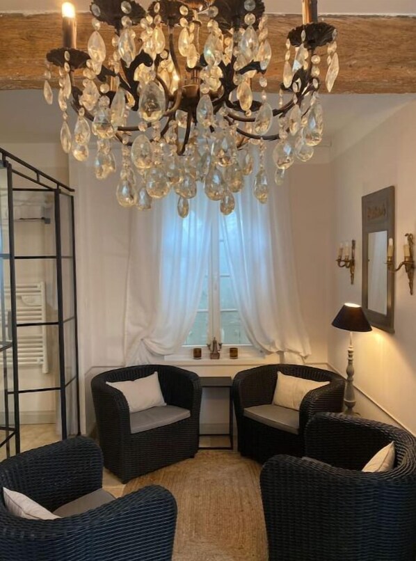 Une pièce avec un lustre, deux fauteuils en osier, une petite table et une fenêtre avec des rideaux.
