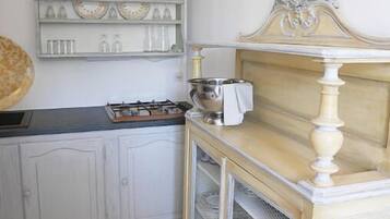 Una cocina con armarios blancos, una estufa a gas y un mueble decorativo con espejo y repisas.