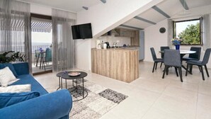 Ein modernes Wohnzimmer mit blauem Sofa, einem kleinen runden Tisch und einer Küchenzeile mit Bar und Esstisch.