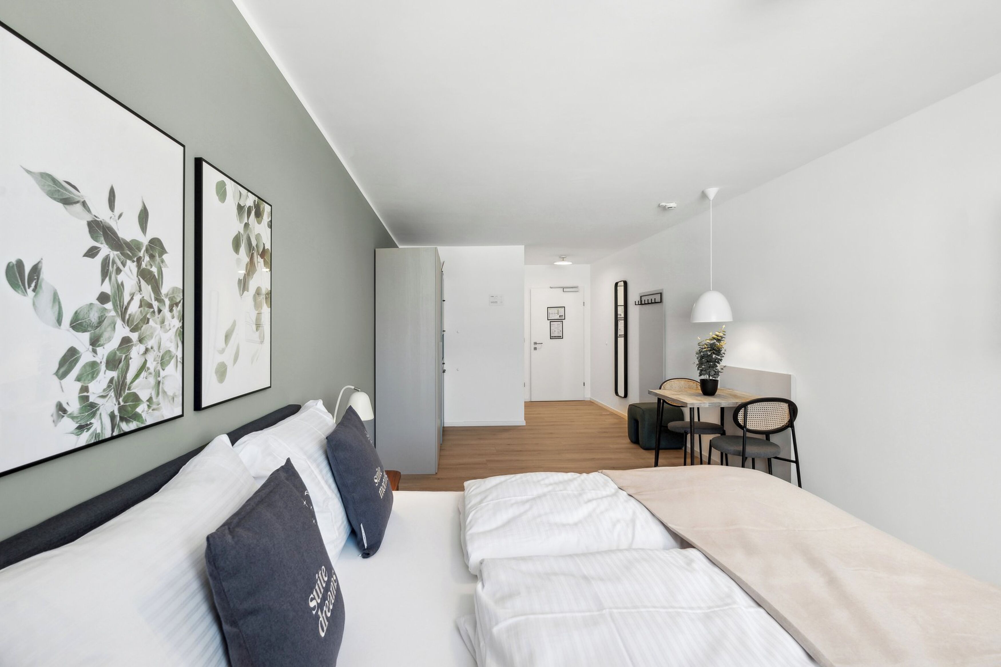 A modern hotel room with a bed, bedside tables, a desk with chairs, and framed artwork on the wall.