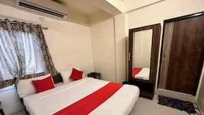 A hotel room with a large bed, a wardrobe, a mirror, and an air conditioning unit. - Hotel Kalyan Palace (Ahmedabad)