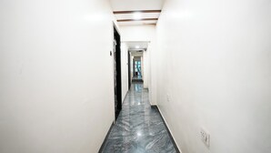 A narrow hallway with white walls and a marble floor. - Hotel Versova Inn (Mumbai)