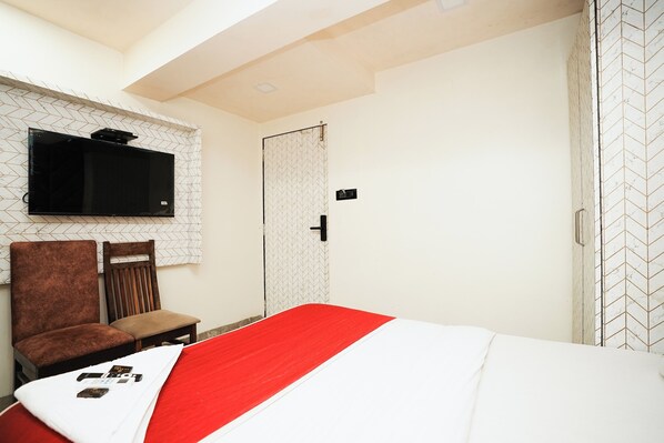 A bedroom with a bed, a TV mounted on the wall, a chair, and a wardrobe.