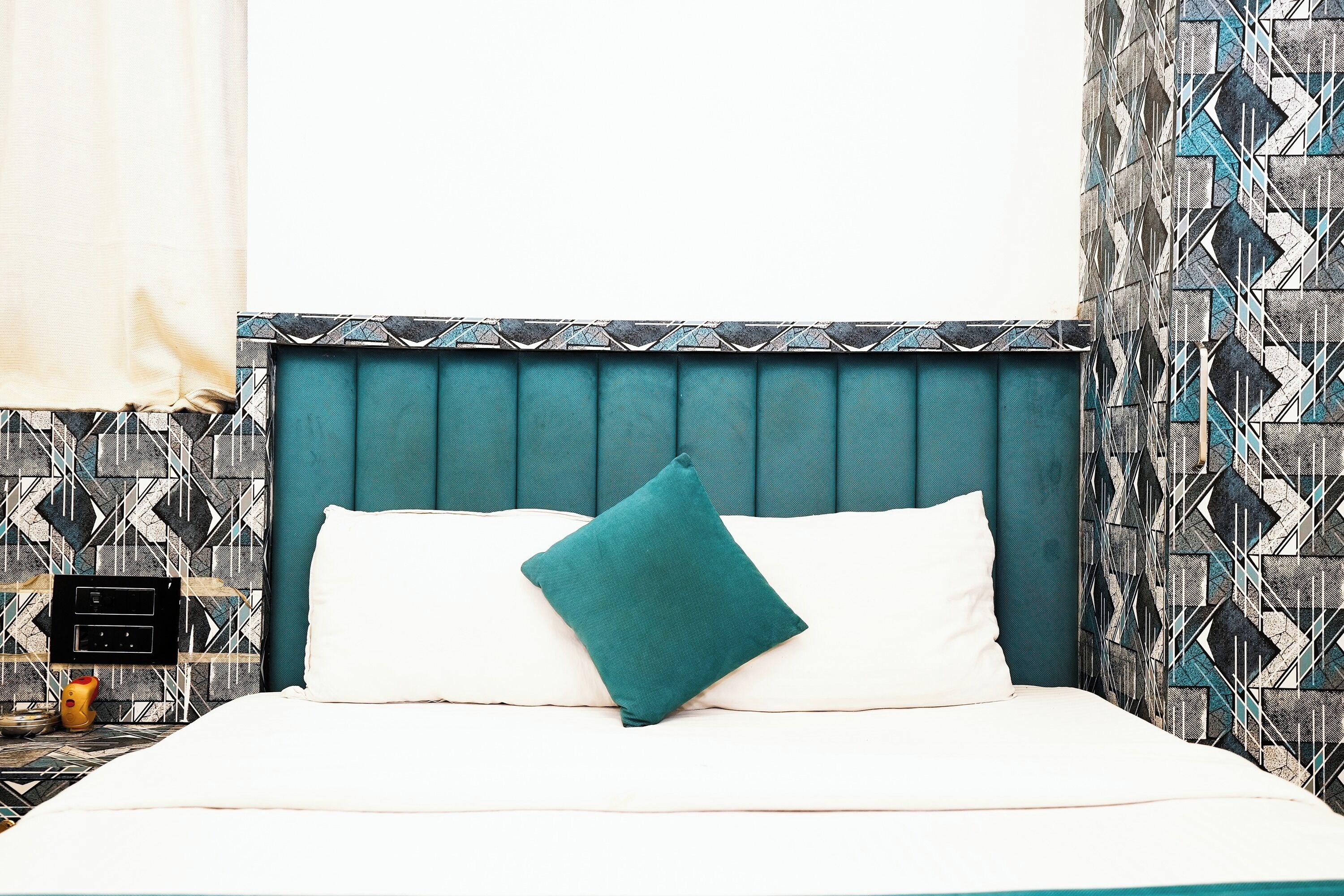 A bed with a teal headboard, white pillows, and a teal throw pillow.