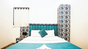 A hotel room with a bed, a nightstand, a window with a curtain, and a wall with a geometric pattern. - Hotel Versova Inn (Mumbai)