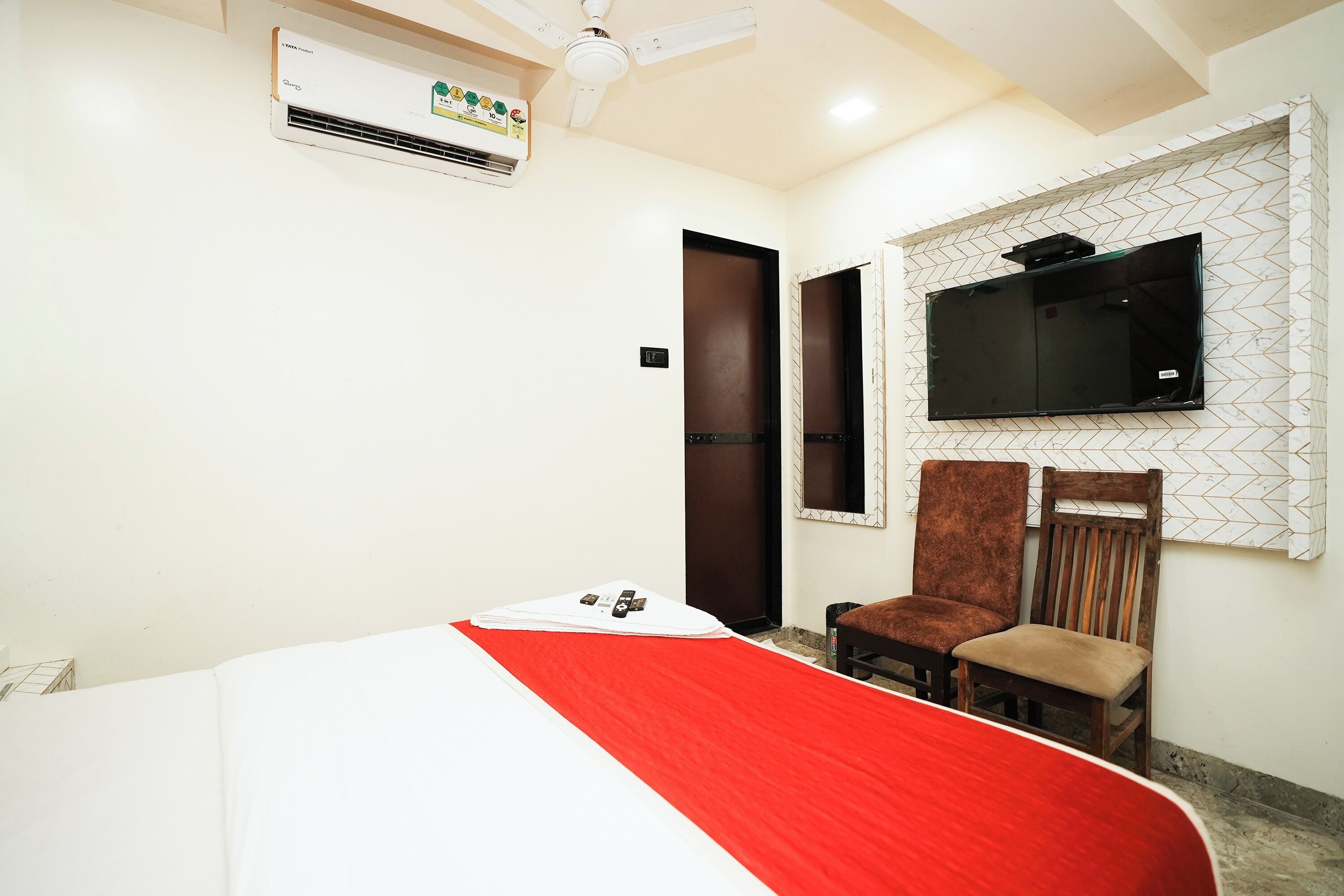 Quarto de hotel com cama, televisão na parede, duas cadeiras e ar condicionado.