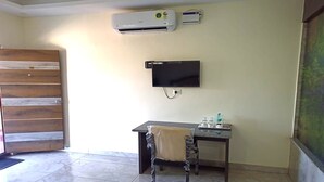 Una habitación con puerta de madera, un escritorio con silla, un televisor y dos unidades de aire acondicionado en la pared.