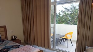 Un dormitorio con una cama, una mesita de noche con hervidor y vistas a un espacio exterior con mesa y sillas.