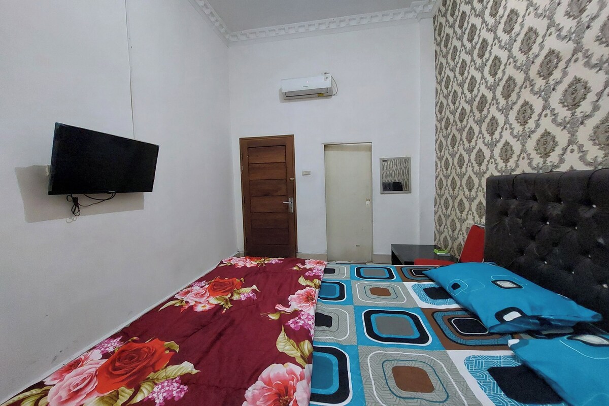 Un dormitorio con una cama, un televisor montado en la pared, una puerta y papel tapiz estampado.