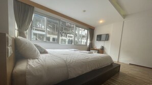 A modern hotel room with a large bed, a flat-screen TV mounted on the wall, and a window with blinds. - Landmark Patong Hotel (Patong)