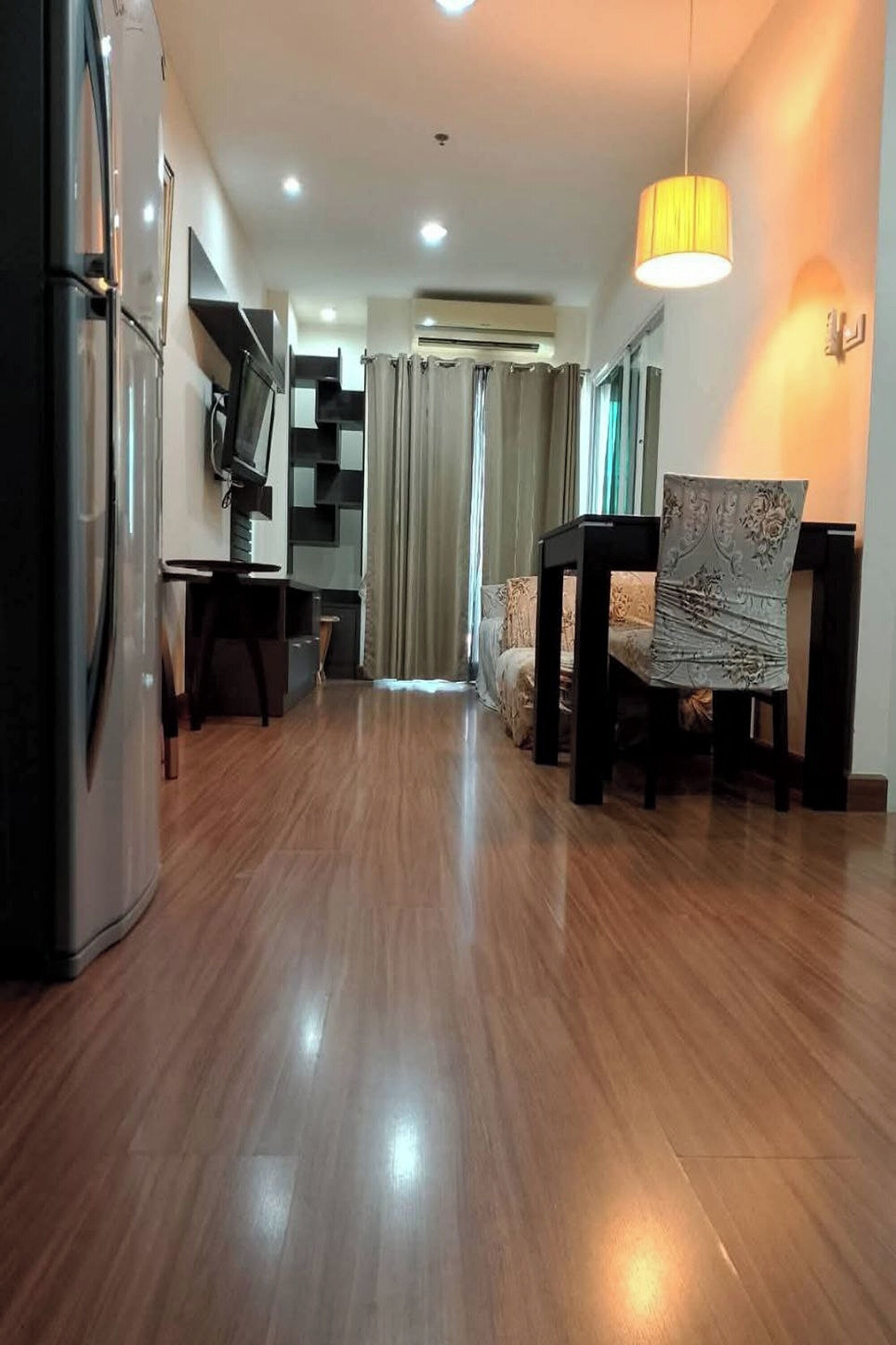 A modern living room with a wooden floor, a dining table with chairs, a sofa, a TV, and a ceiling light.