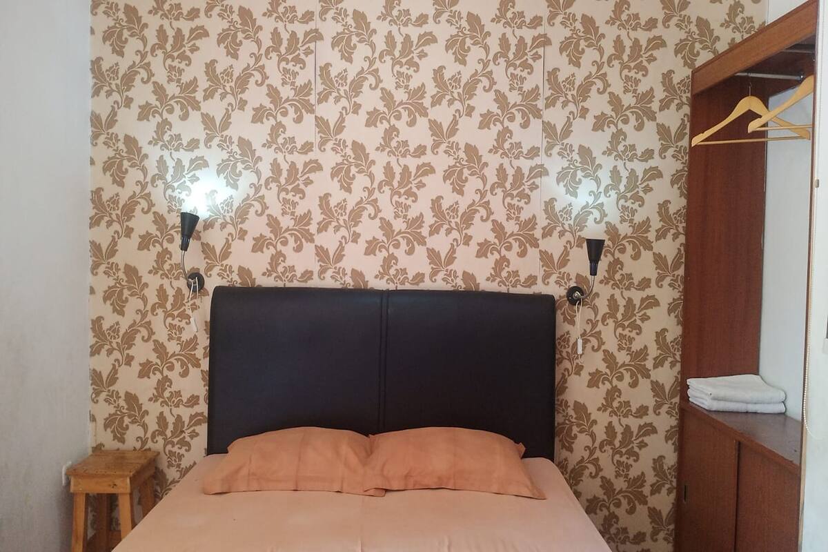 A bed with a black headboard, a wooden side table, and a wardrobe with a hanging rack.