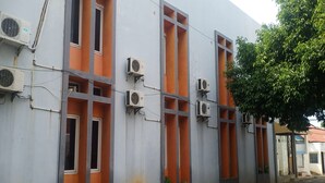 A building with multiple air conditioning units attached to the exterior walls, windows with orange frames, and a brick-paved ground. - Aryani Suites Syariah (Jakarta)