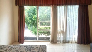 A room with a bed, a window with curtains, and a view of greenery outside. - Aryani Suites Syariah (Jakarta)