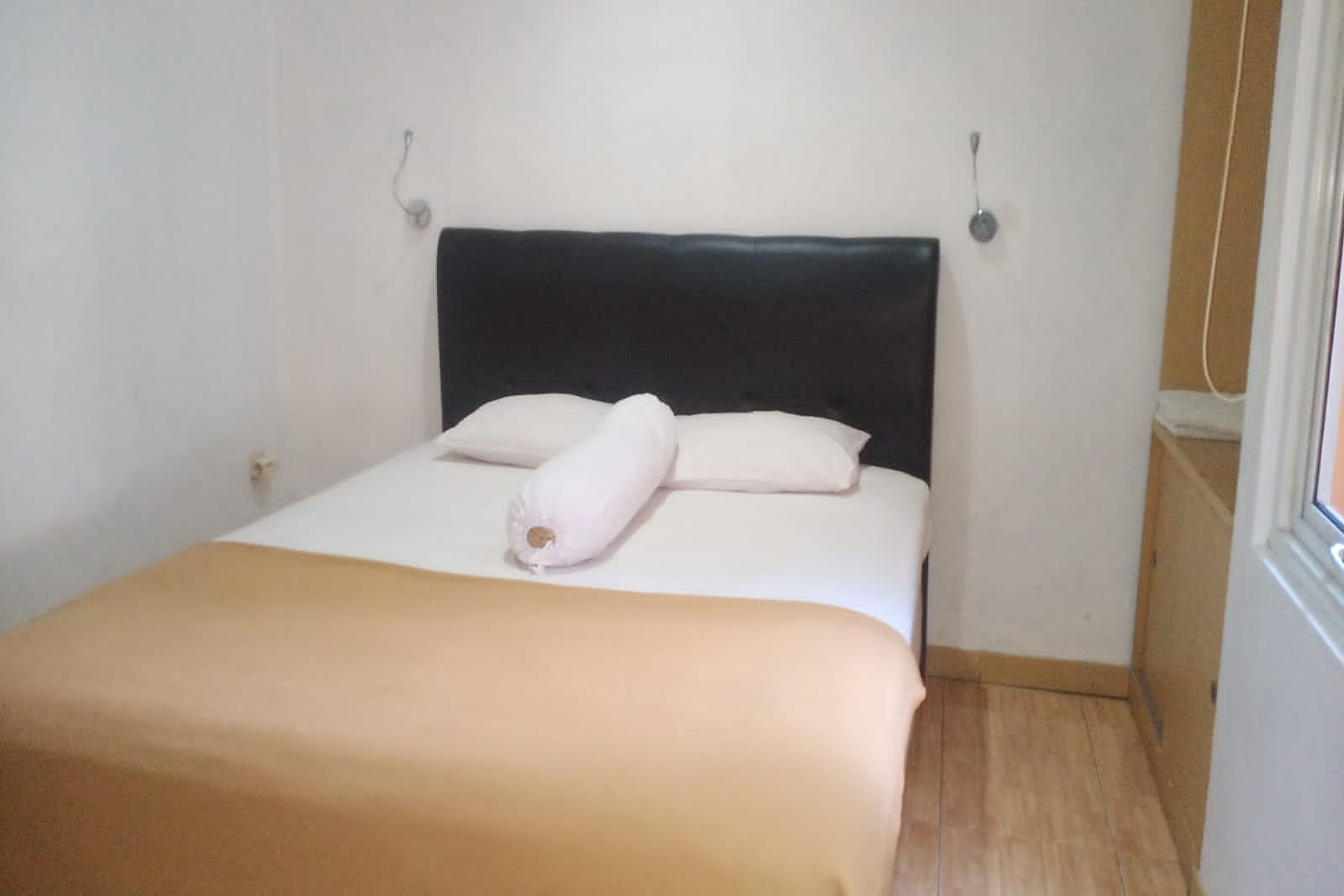 Una cama pequeña y ordenada con cabecera oscura, almohadas blancas y manta color beige.