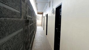 A corridor with stone walls and a tiled floor, leading to a black door. - Aryani Suites Syariah (Jakarta)