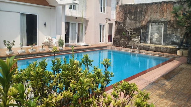 A swimming pool surrounded by potted plants and a building with multiple windows and doors. - Aryani Suites Syariah (Jakarta)