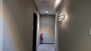 Un pasillo estrecho con un extintor montado en la pared, una luz de techo y una alfombra texturizada.
