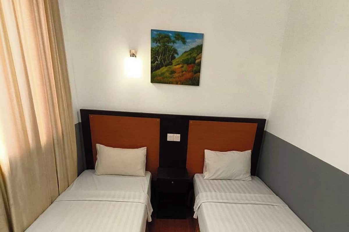 Ein Hotelzimmer mit zwei Einzelbetten, einem Nachttisch dazwischen, einem Bild an der Wand und einem Fenster mit Vorhängen.