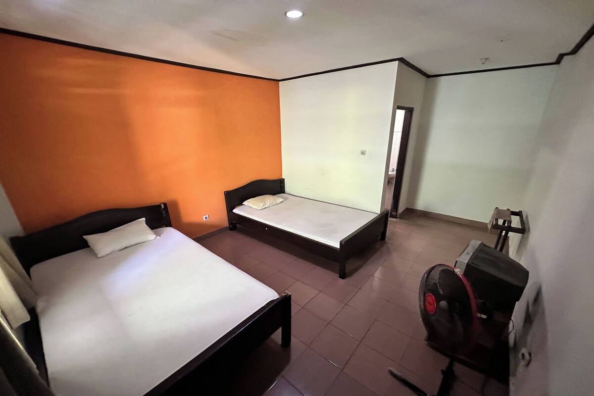 A hotel room with two single beds, a standing heater, and a door leading to another room.
