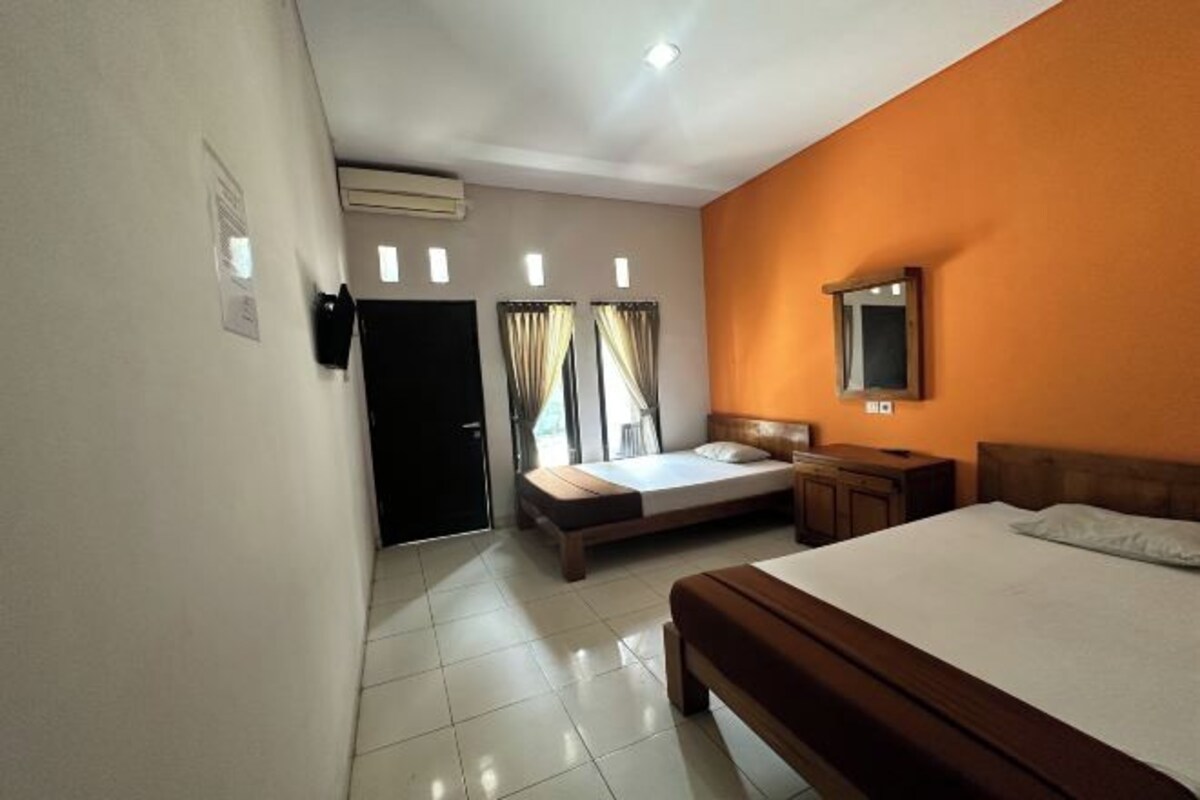 A hotel room with a bed, a bedside table, a mirror, a window with curtains, and an air conditioning unit.