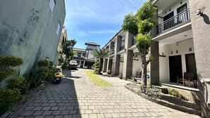 A paved street lined with buildings, a scooter parked on the side, and a clear blue sky. - Hotel Warta Sari (Denpasar)