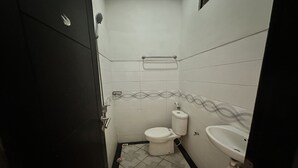 A small, tiled bathroom with a toilet, sink, and a towel rack. - Hotel Warta Sari (Denpasar)