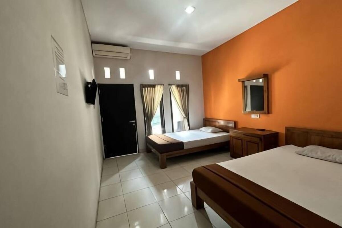 A hotel room with a bed, a desk, a chair, a mirror, and a door.