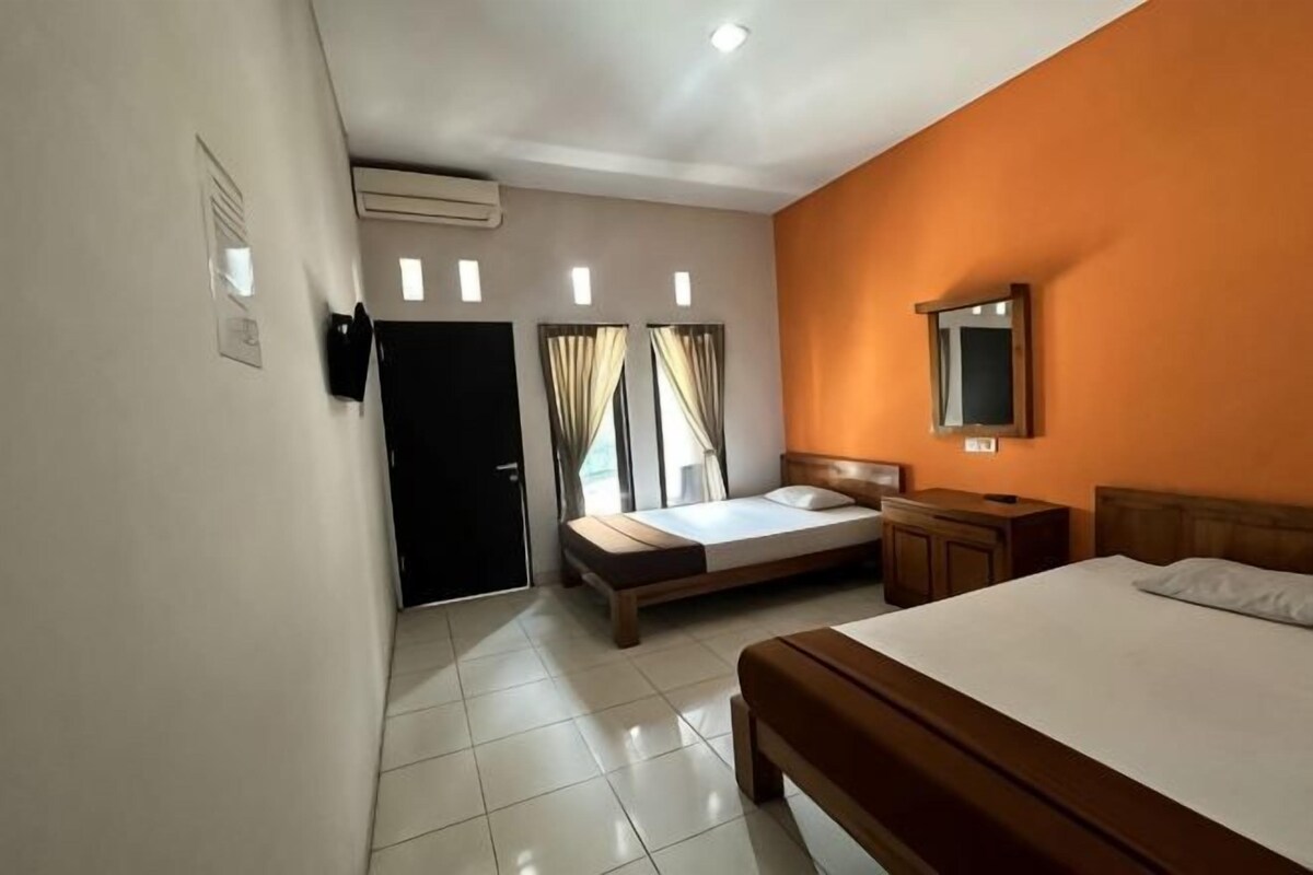 A hotel room with a bed, a desk, a chair, a mirror, and a door.