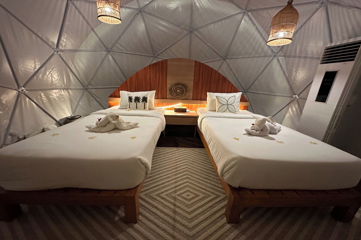 A cozy, tent-like room with two beds, a central table, and decorative pillows.