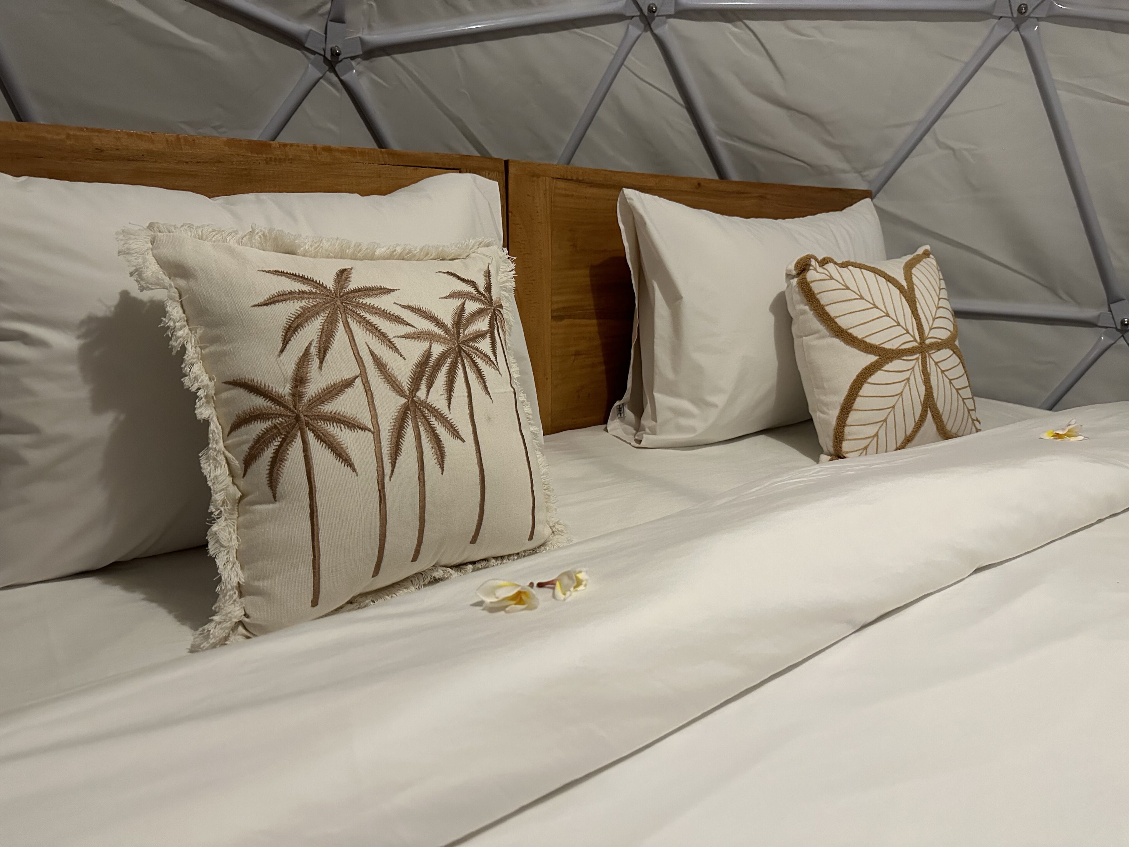 A bed with two pillows, one with palm tree designs and the other with a leaf pattern, in a tent-like room.