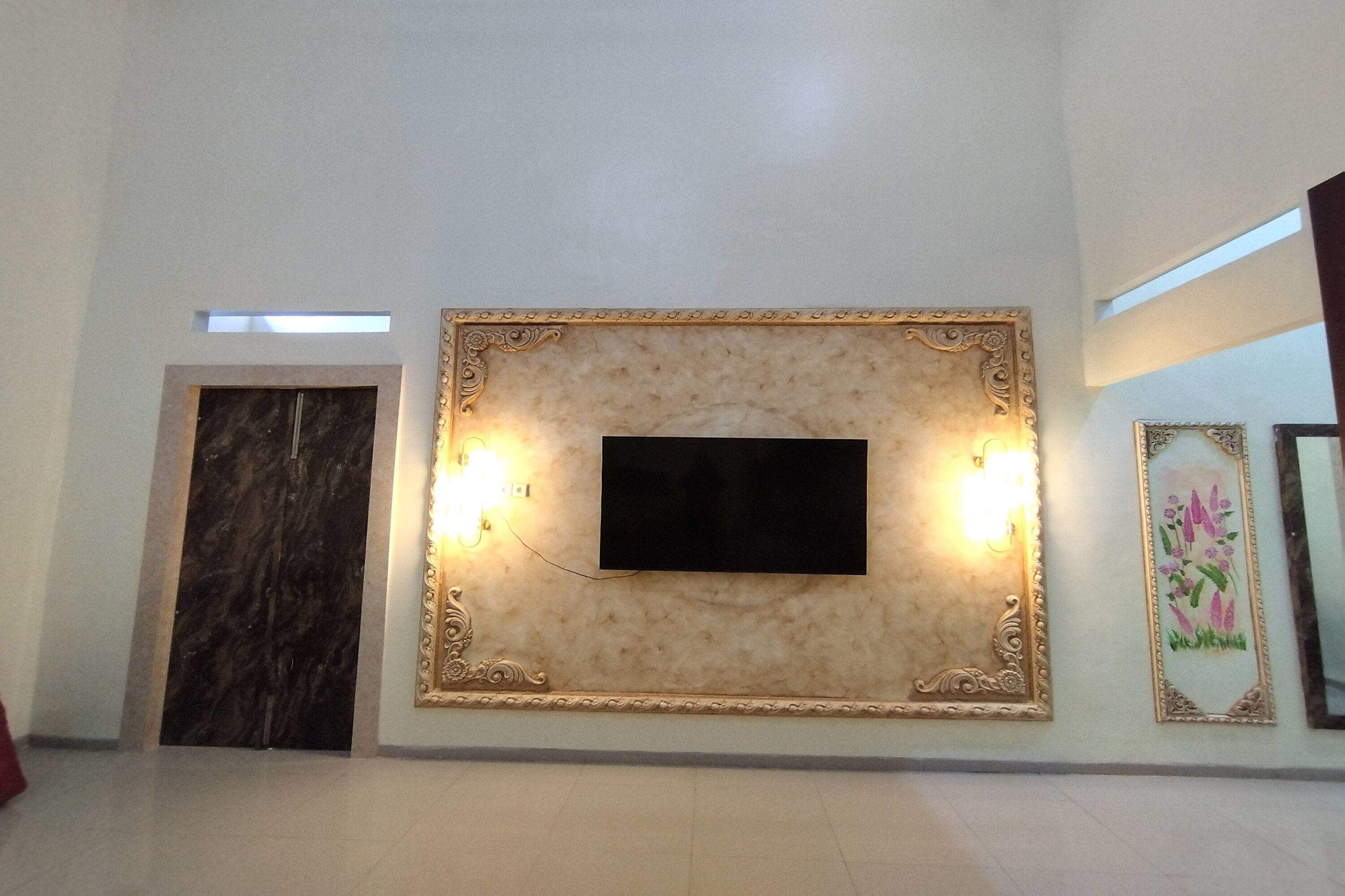 Una habitación con pared de mármol, un televisor de pantalla plana y dos lámparas de pared.