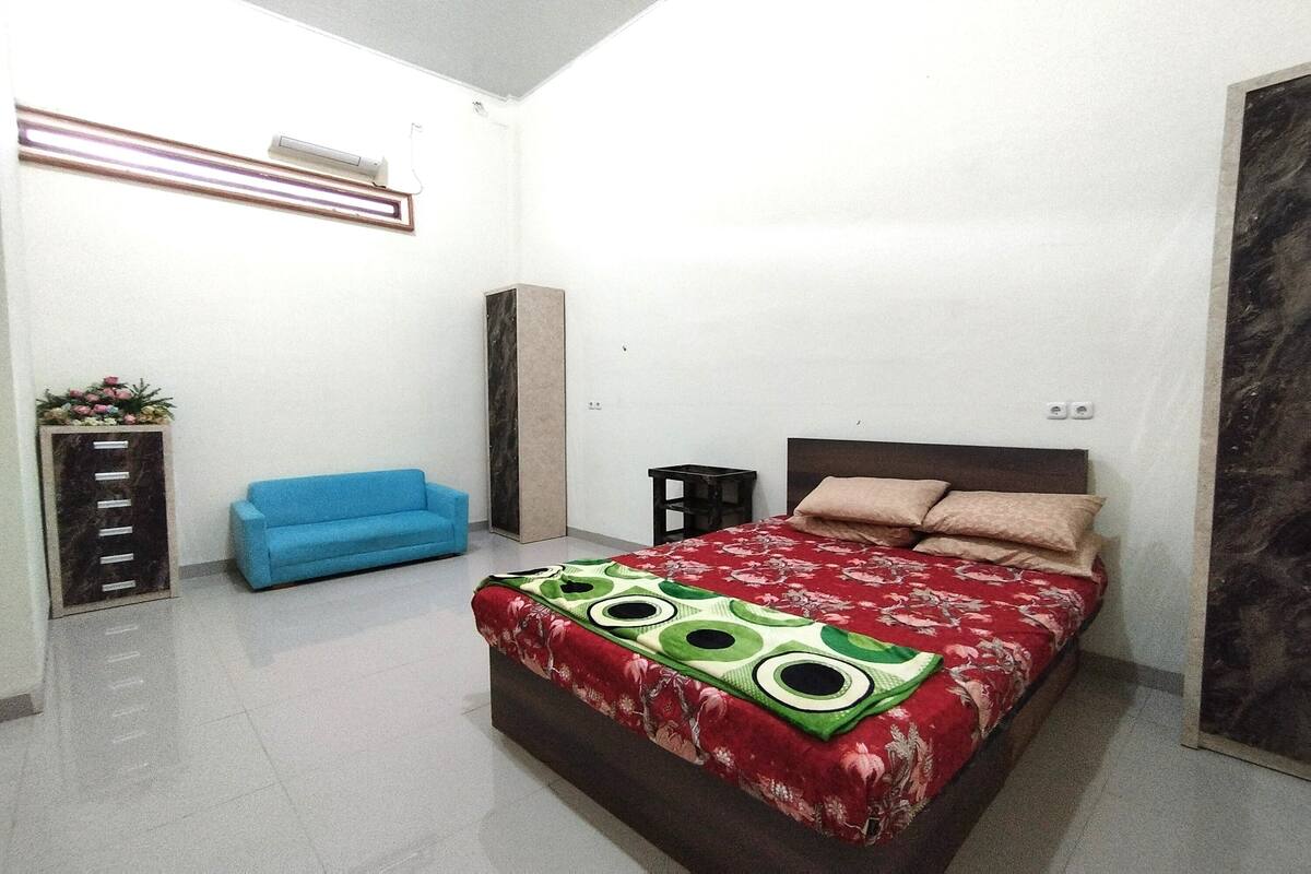 Un dormitorio con cama, sofá azul, un armario alto y aire acondicionado instalado en la pared.