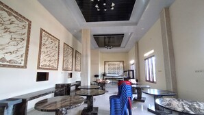 A spacious lobby with marble-topped tables and chairs, a central column, and framed artwork on the walls. - Zahira Guesthouse Syariah (Jambi)